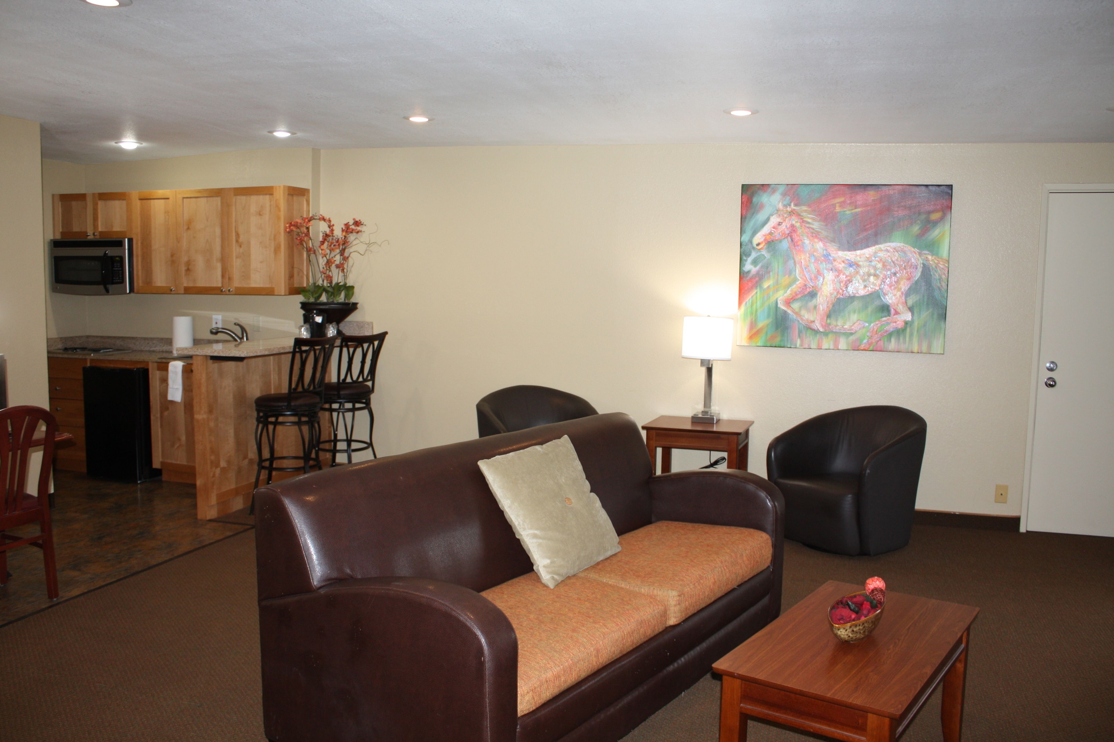 A living room with a brown leather sofa, a wooden coffee table, and a painting of a horse on the wall.