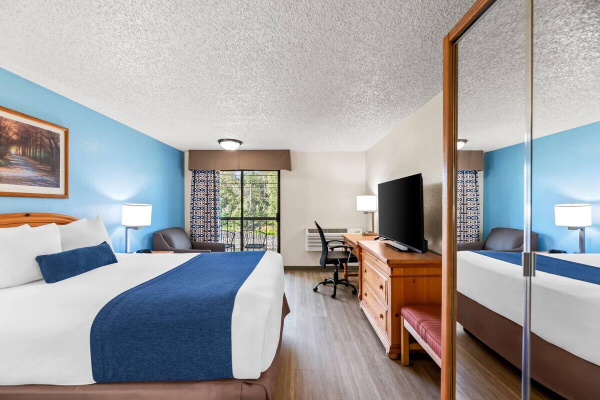 Une chambre d’hôtel avec un grand lit, un bureau avec un ordinateur, une télévision et une fenêtre avec des rideaux.