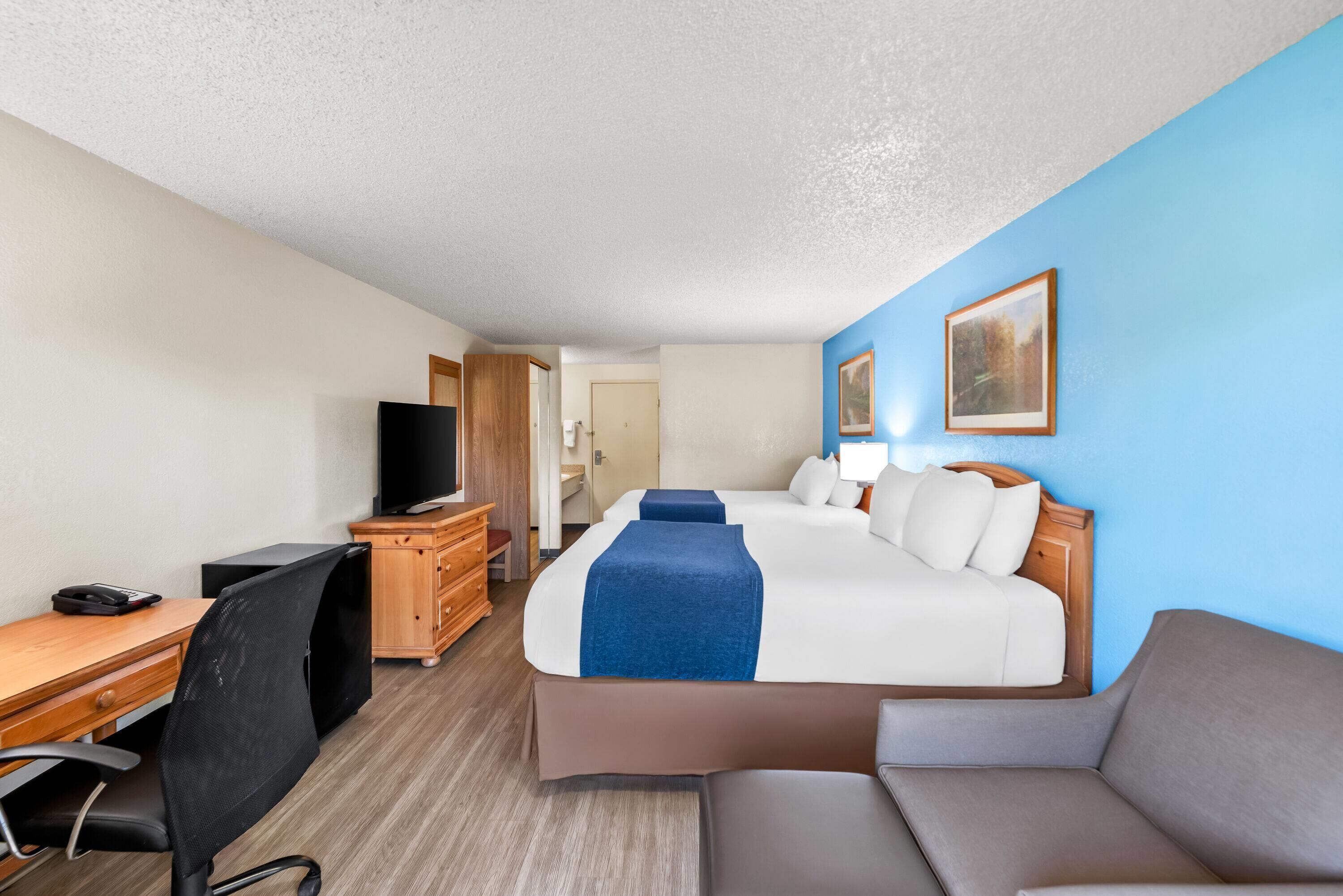 Quarto de hotel com cama, escrivaninha, cadeira, televisão e sofá.