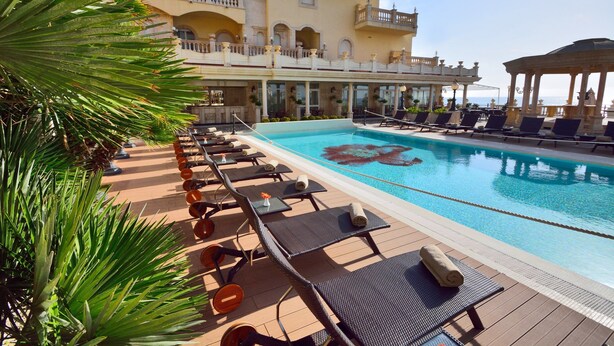 Zona junto a la piscina con sillones de descanso, piscina y un edificio con balcones.