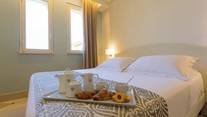 Una habitación de hotel con una cama bien hecha, una bandeja con pasteles y un calentador de agua, y una ventana con cortinas.