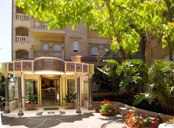 L’entrée d’un hôtel, agrémentée d’une arche décorative, de plantes en pot et d’un jardin où poussent des plantes et des fleurs tropicales.