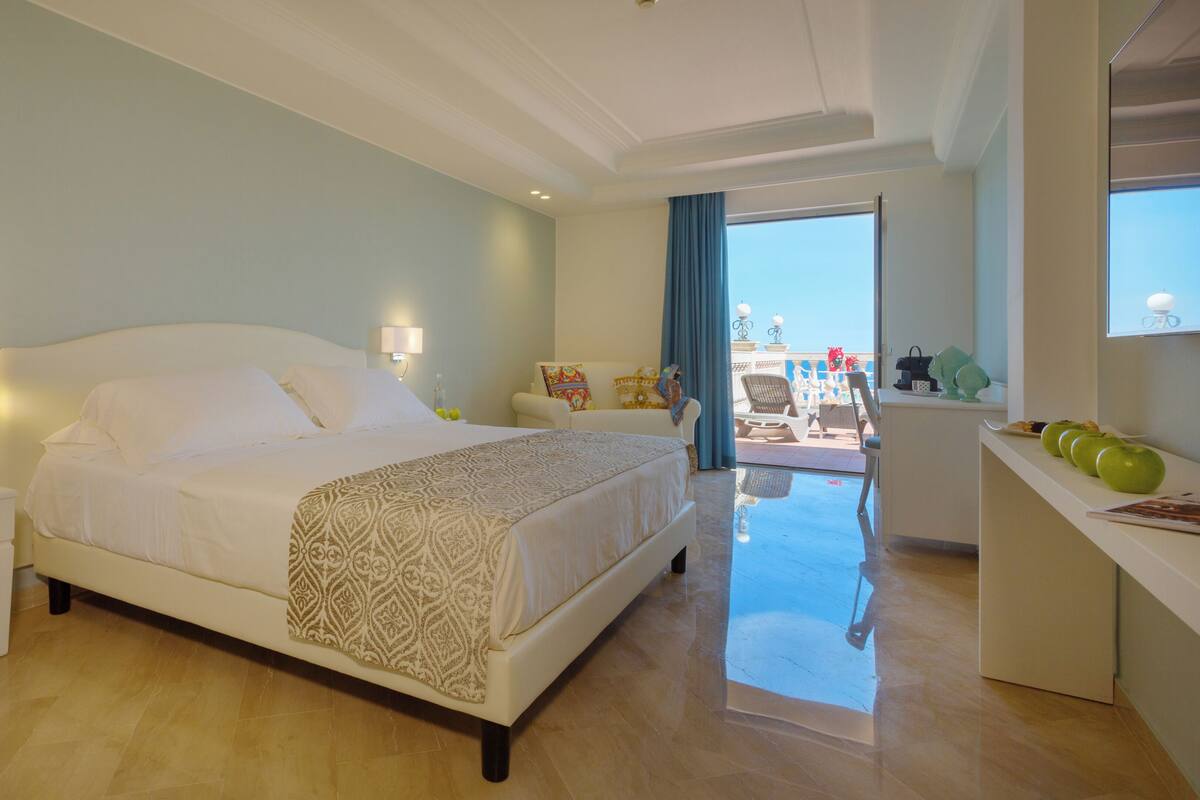 Een moderne hotelkamer met een groot bed, nachtkastjes, een bureau met appels en een balkon met tuinmeubilair.