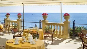 Una terraza al aire libre con mesas y sillas redondas, con vistas al mar.