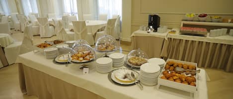 A buffet setup with various food items and a seating area with white chairs and tables.