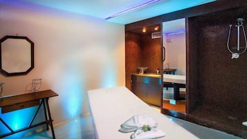 Relax in a serene spa room with a massage table, desk, and mirror.