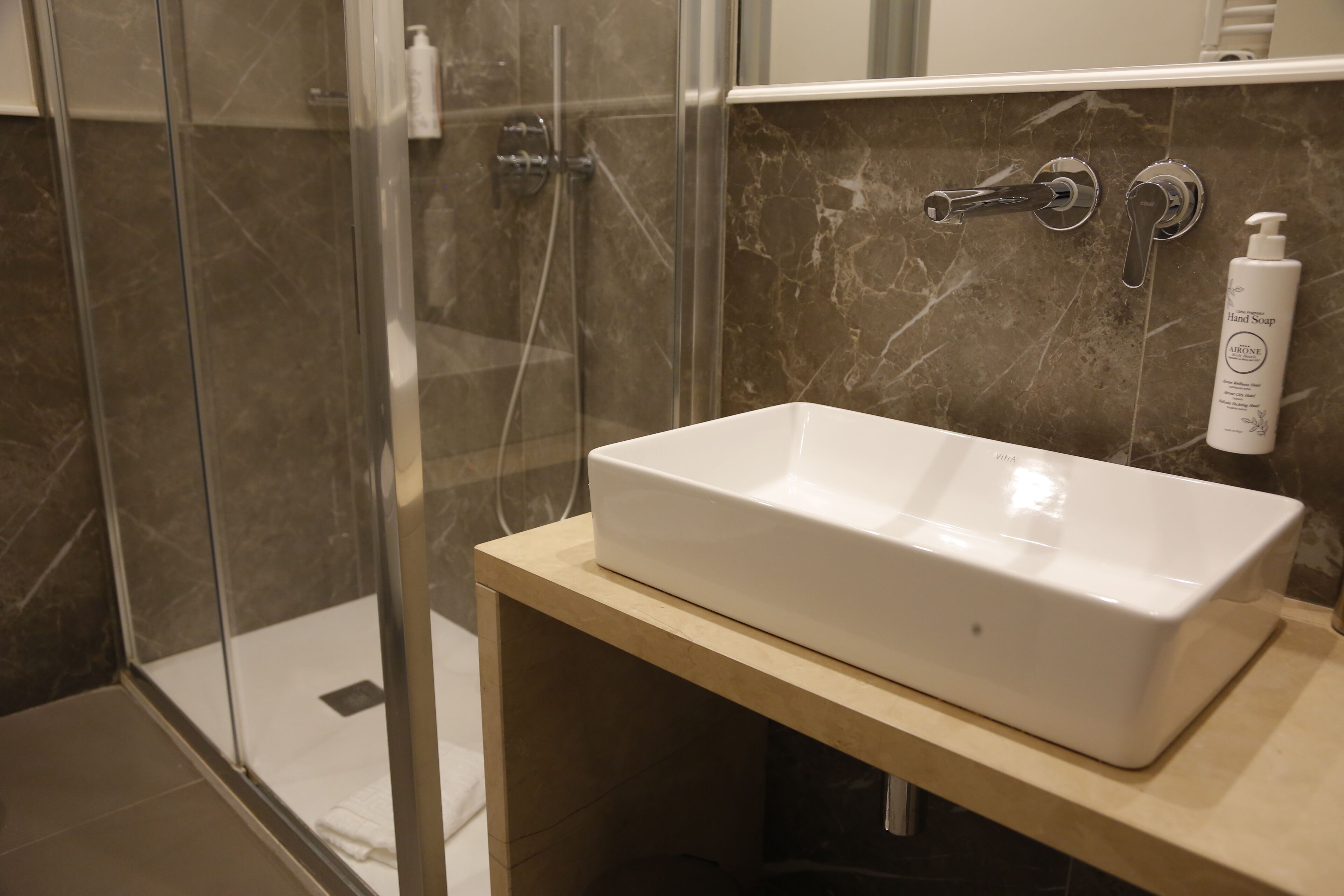 A bathroom with a white sink, a glass shower enclosure, and a marble-tiled wall.