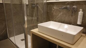 A bathroom with a white sink, a glass shower enclosure, and a marble-tiled wall.