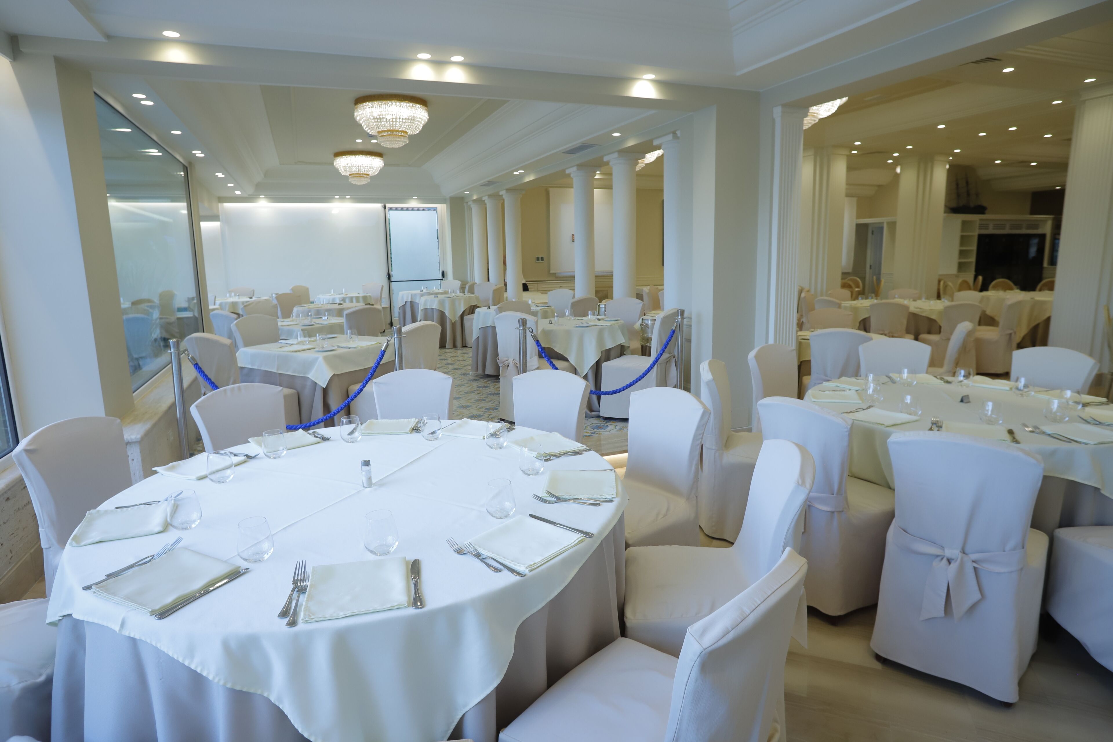 Une salle de banquet avec des tables rondes, des chaises blanches et des cordes bleues.