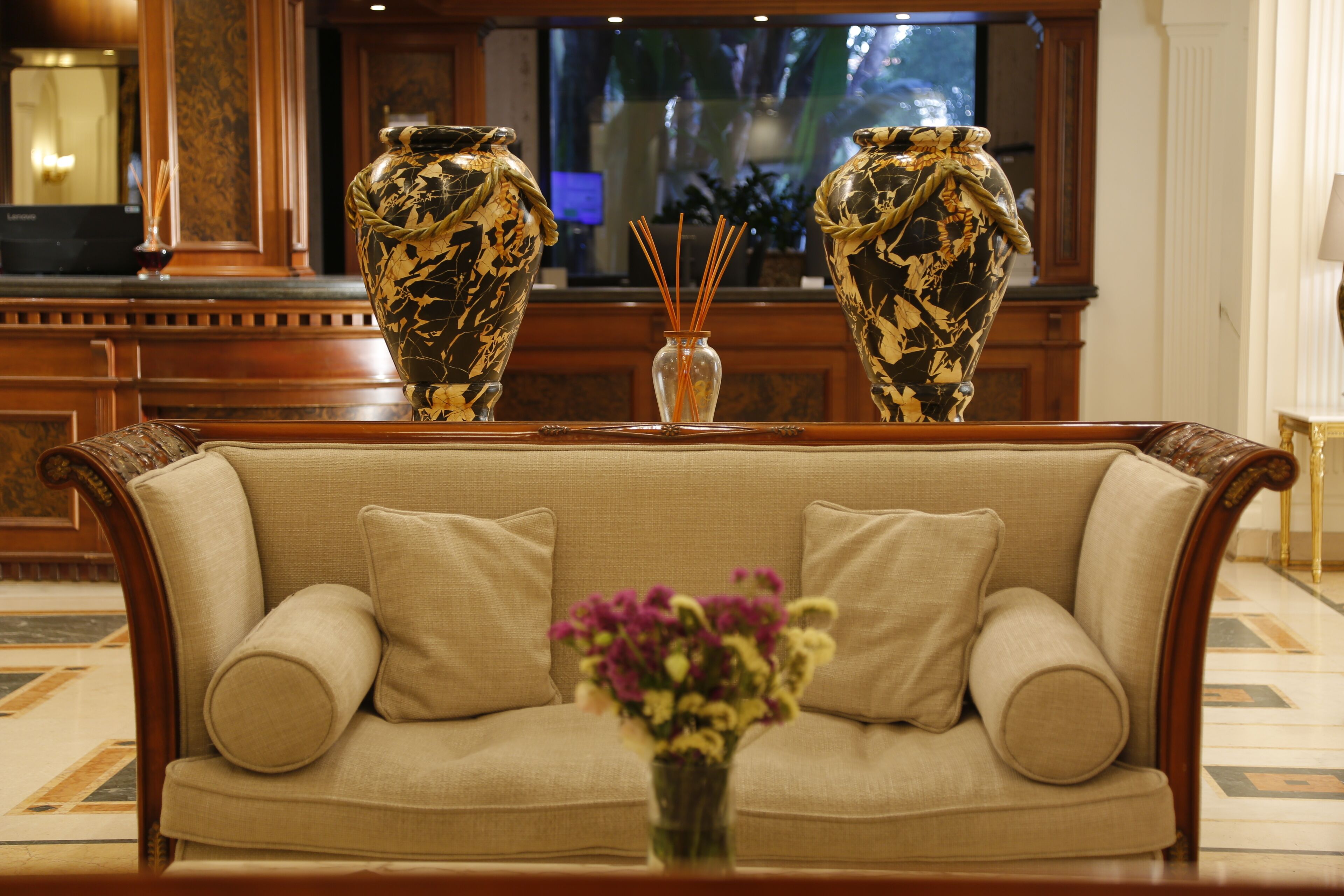 Un canapé beige avec deux coussins, un vase avec des fleurs violettes et deux vases décoratifs ornés d’un motif de feuilles, le tout posé sur une table en bois.