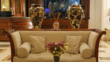 Un canapé beige avec deux coussins, un vase avec des fleurs violettes et deux vases décoratifs ornés d’un motif de feuilles, le tout posé sur une table en bois.