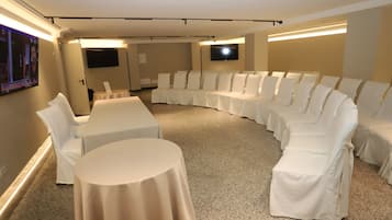Un salón de conferencias con una mesa blanca curva y sillas, piso alfombrado y una pantalla plana montada en la pared.
