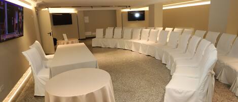 Une salle de conférence dotée d’une table et de chaises blanches aux lignes courbes, d’un sol recouvert de moquette et d’un téléviseur à écran plat fixé au mur.