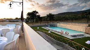 Un área de comedor en la azotea con mesas dispuestas para una comida, una piscina y vistas del paisaje circundante.