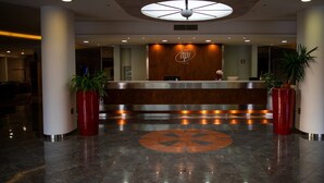 Zona de recepción de un hotel con diseño moderno, que presenta un mostrador central, un gran elemento de iluminación en el techo e igualmente dos plantas en cada lado.