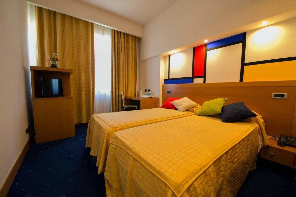 A hotel room with two beds, a desk with a chair, a TV, and a minibar.