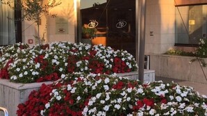 Entrada de hotel con puerta de vidrio, un letrero con el logotipo 'hp' y un cantero con flores rojas y blancas.