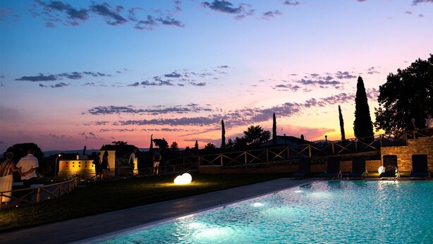 Una piscina con vistas al atardecer, una cerca de madera y algunas personas caminando.