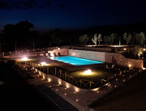 A nighttime swimming pool area with a brick wall, a wooden deck, and a bridge. - Hotel Planet (Arezzo)