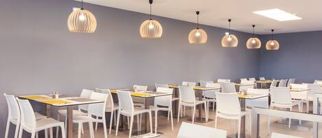 A modern dining area with white tables and chairs, pendant lighting, and a neutral color scheme.