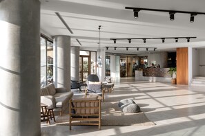 A spacious lobby with large windows, a seating area with sofas and chairs, and a reception desk. - Blue Sky City Beach Hotel (Rhodes)