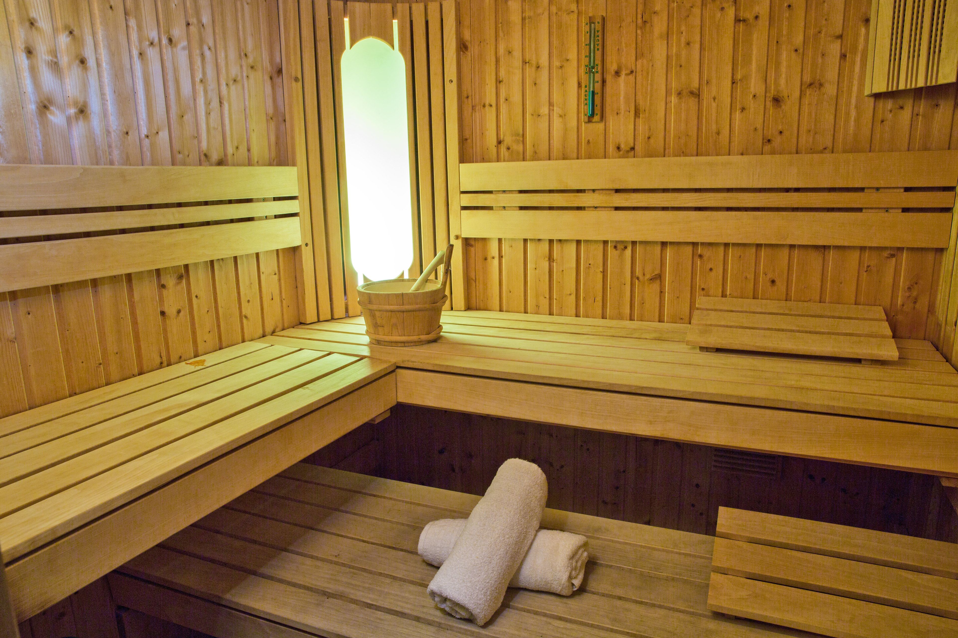 A sauna with wooden benches and benches, a bench with a towel, and a wooden wall with a thermometer.
