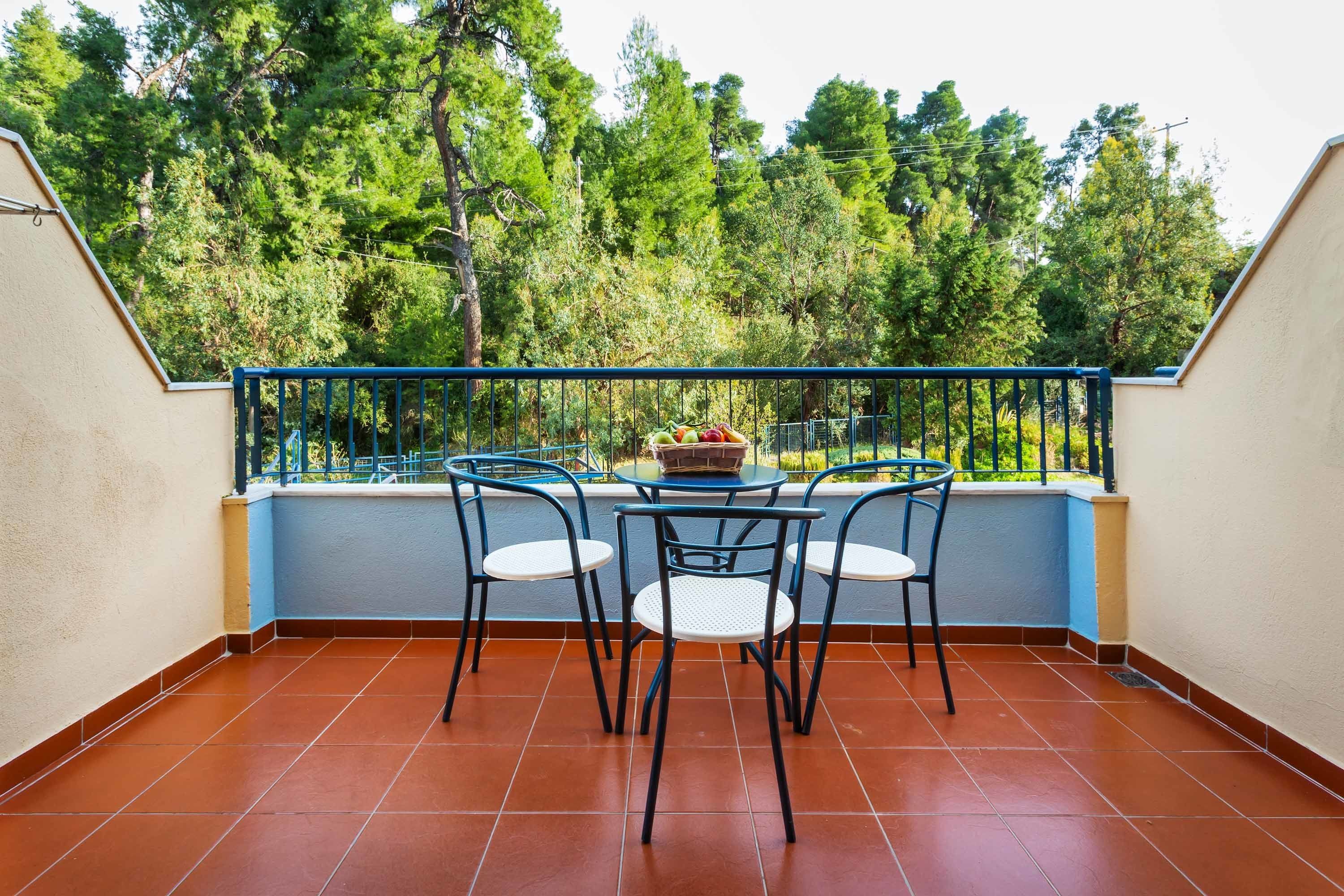 Un balcón con una mesa y sillas, una cesta de fruta y vistas a árboles.
