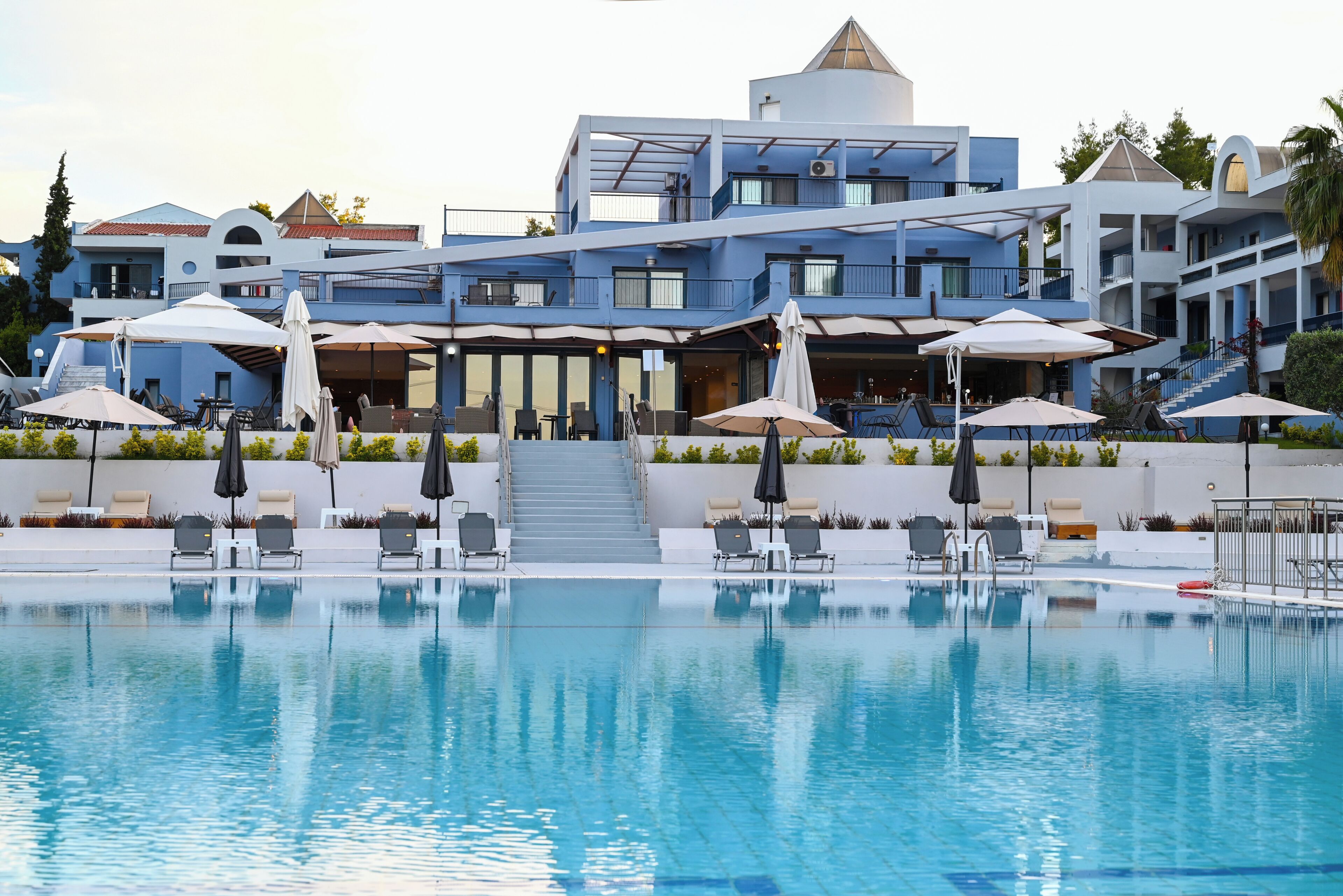 A modern hotel with a swimming pool, outdoor seating, and a staircase leading to the upper floors.