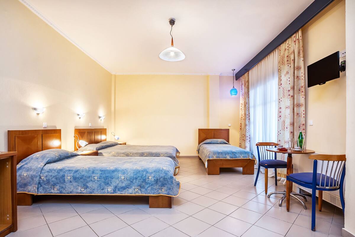 Habitación de hotel con dos camas individuales, un escritorio con silla, un televisor de pantalla plana y una ventana con cortinas.