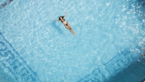 A person floating in a clear blue pool with a tiled floor.