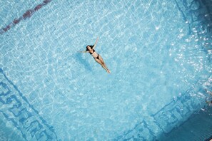 A person floating in a clear blue pool with a tiled floor.