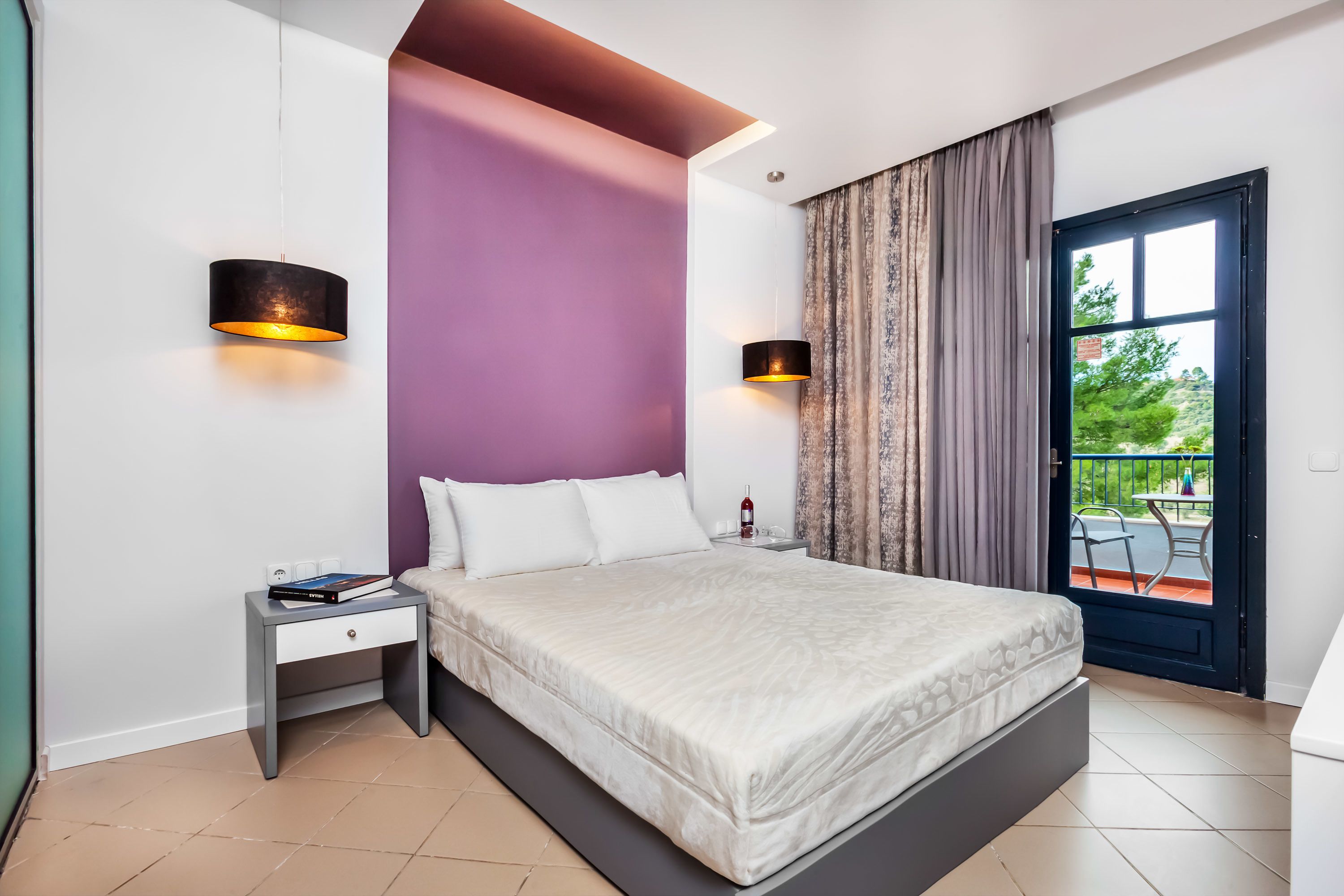 Ein modernes Schlafzimmer mit einem großen Bett, zwei Nachttischen, einem Beistelltisch und Blick ins Freie durch eine Schiebetür.