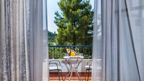 A balcony with a table set for two, overlooking a tree and a distant landscape.