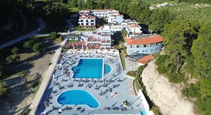 Vue aérienne d’un complexe hôtelier doté d’une grande piscine, de plusieurs bâtiments et entouré d’un paysage naturel.
