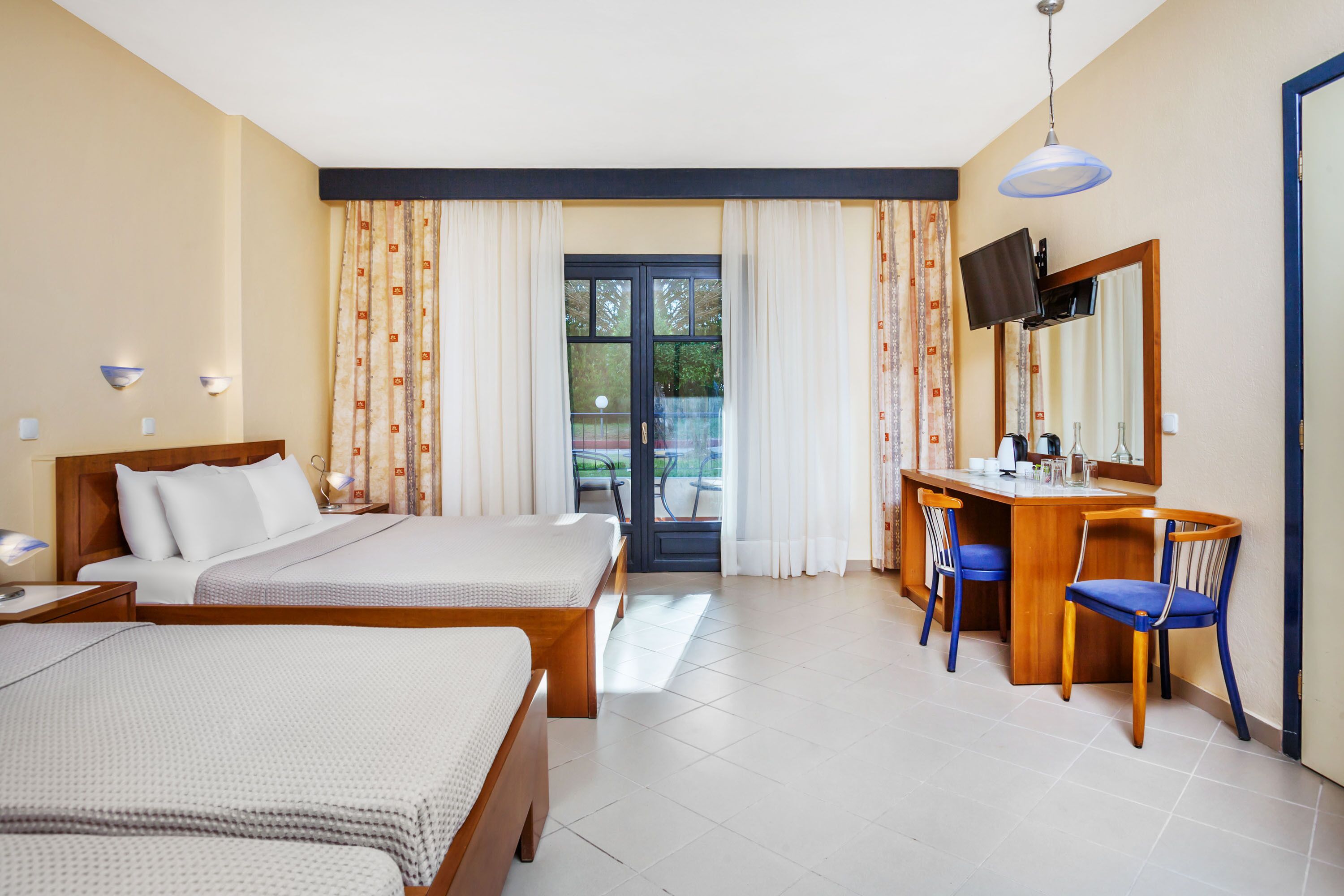 Una camera d'albergo con due letti, una scrivania con una sedia, una televisione e un'ampia finestra con tende.