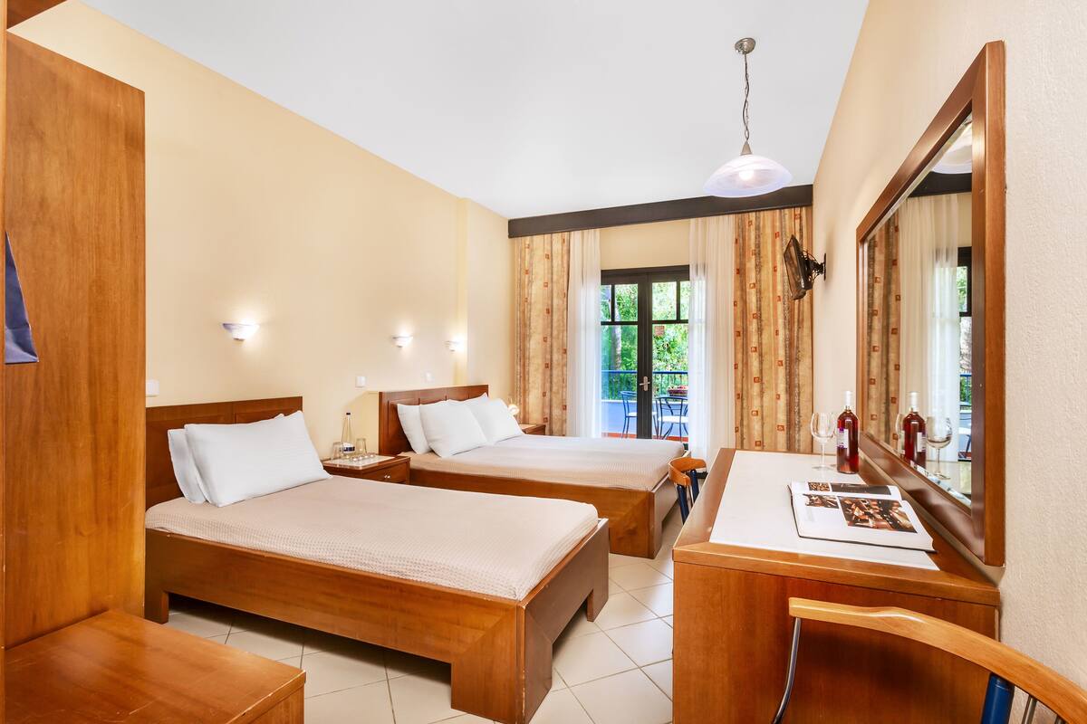 Habitación de hotel con dos camas de madera, un escritorio con silla, un espejo y una ventana con cortinas.