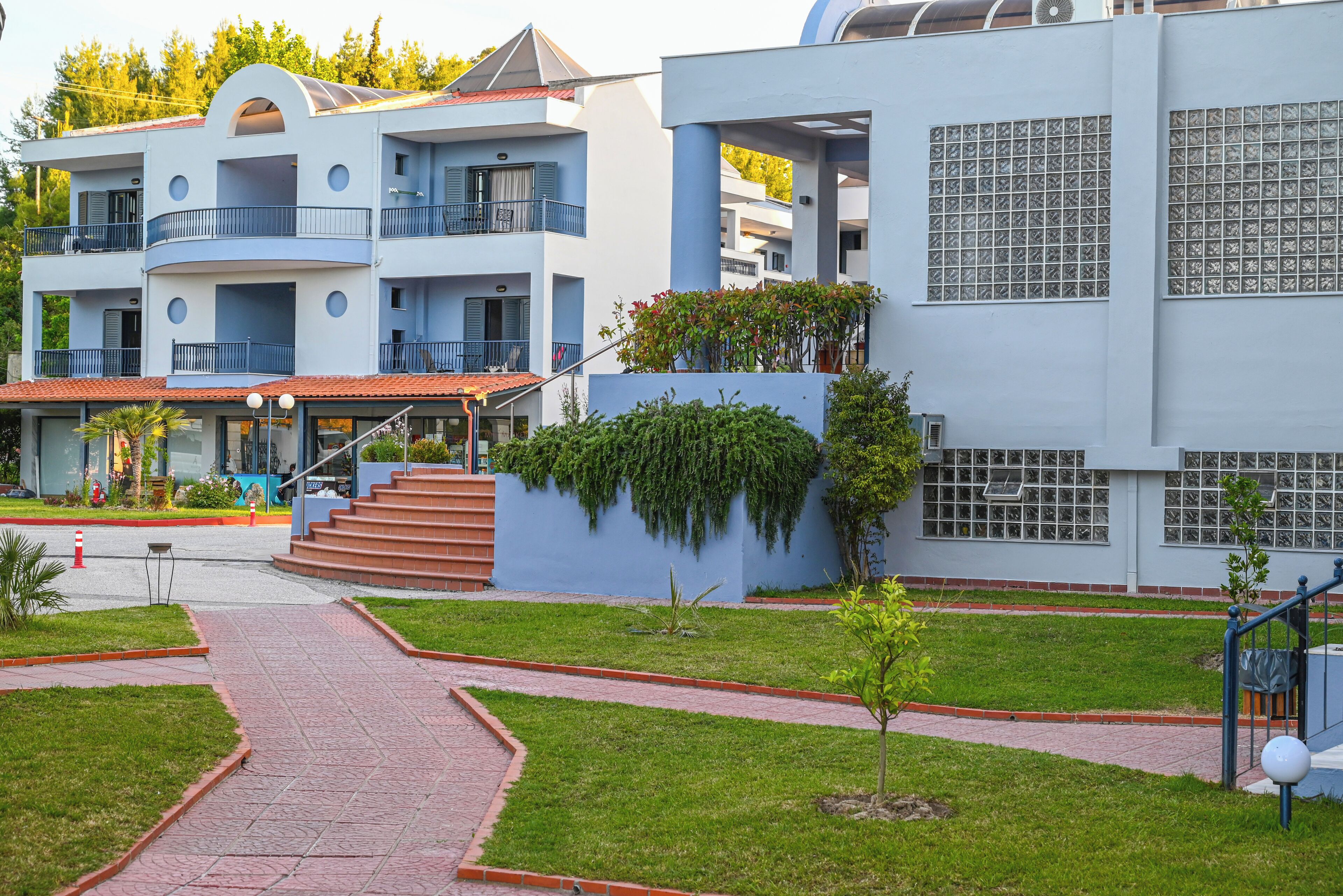 A modern building with multiple balconies, a central staircase, and a paved walkway.