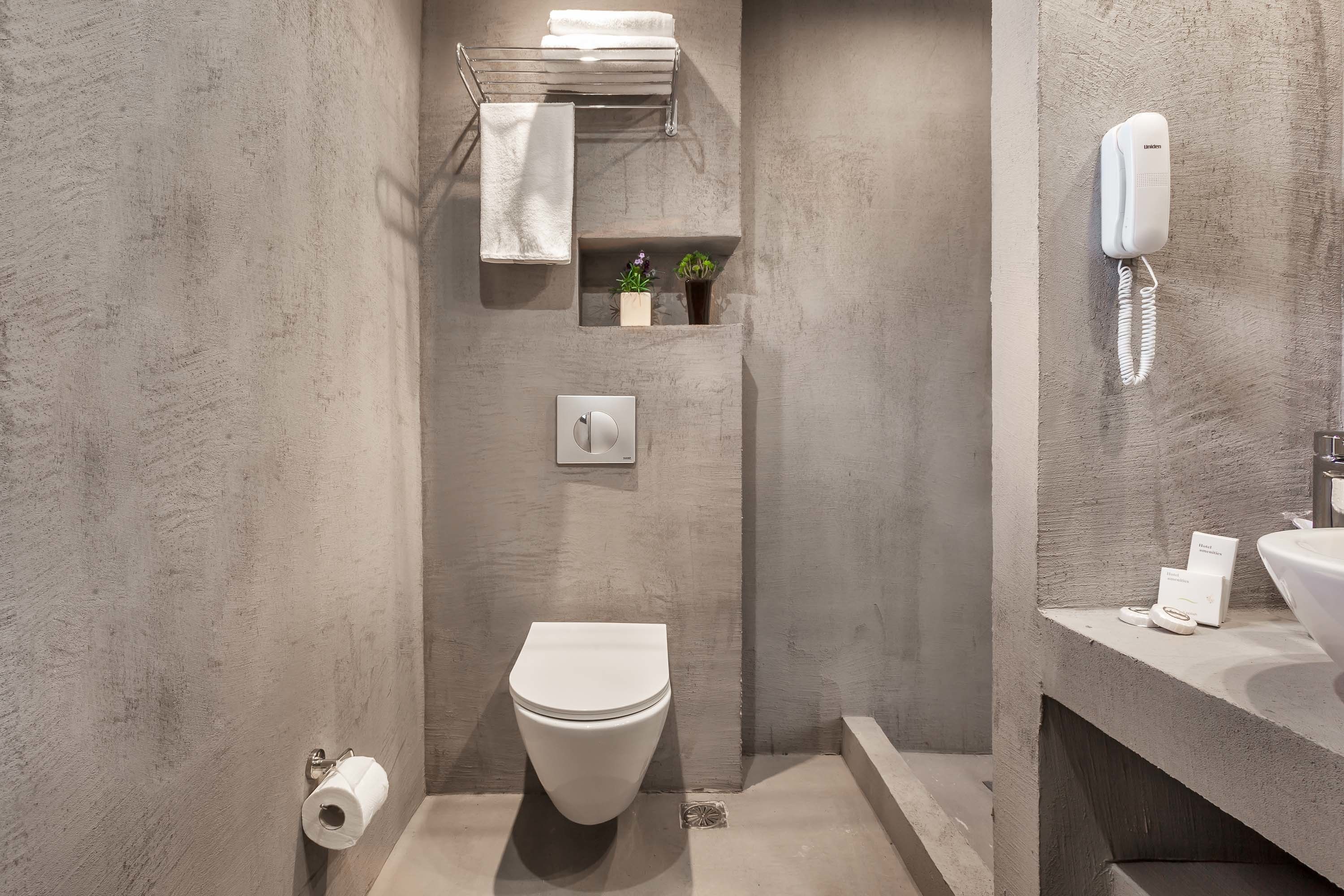 A modern bathroom with a toilet, towel rack, small shelf with plants, a phone, and a sink.