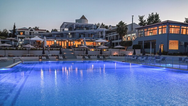 A swimming pool with lounge chairs and umbrellas, surrounded by modern buildings with outdoor seating. - Atrium Hotel (Kassandra)