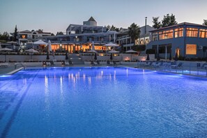 Une piscine entourée de chaises longues et de parasols, elle-même bordée de bâtiments modernes dotés d’espaces de détente en plein air.