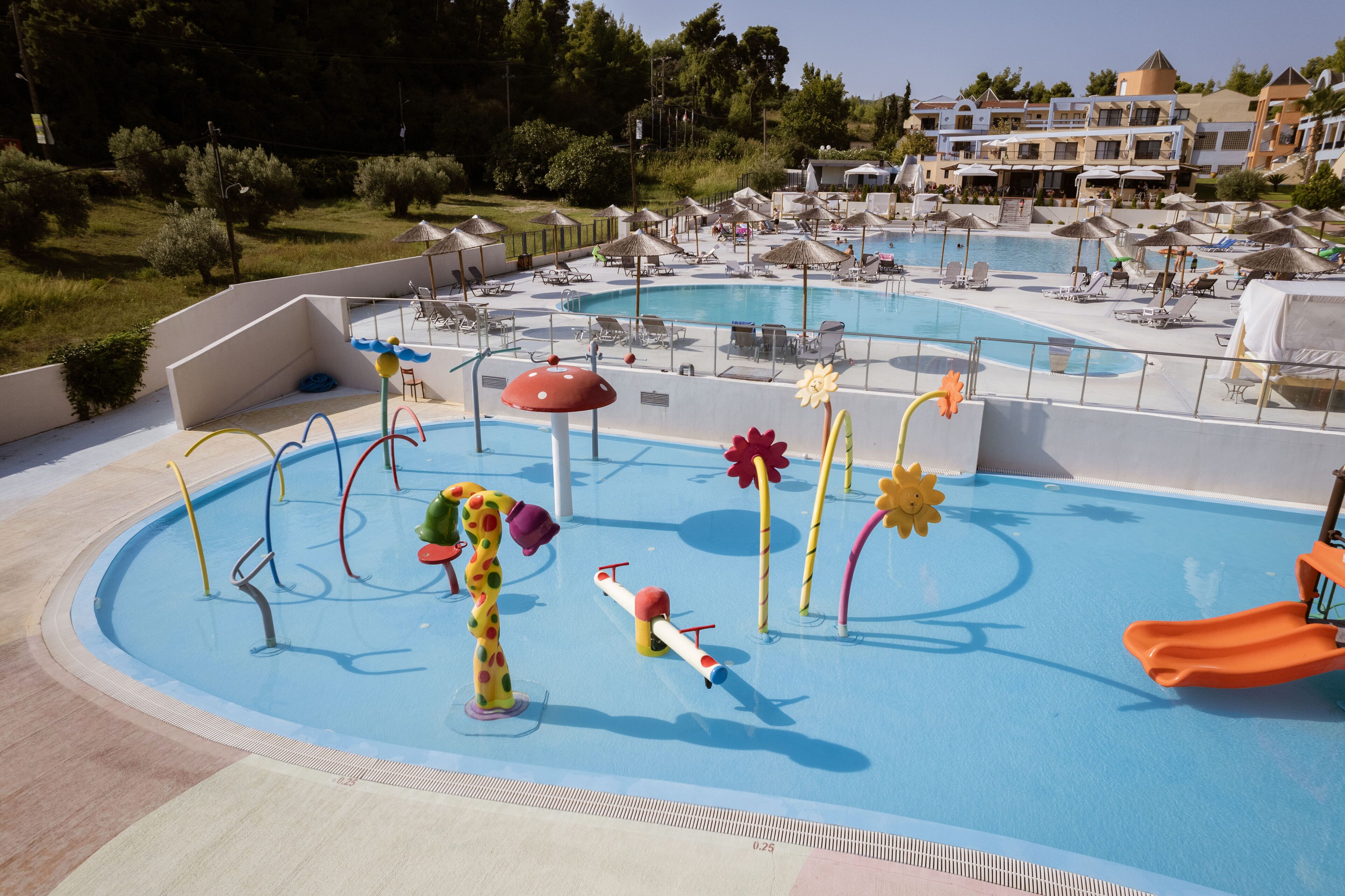 Una piscina con toboganes y estructuras de juego, rodeada de sillas de descanso y sombrillas.