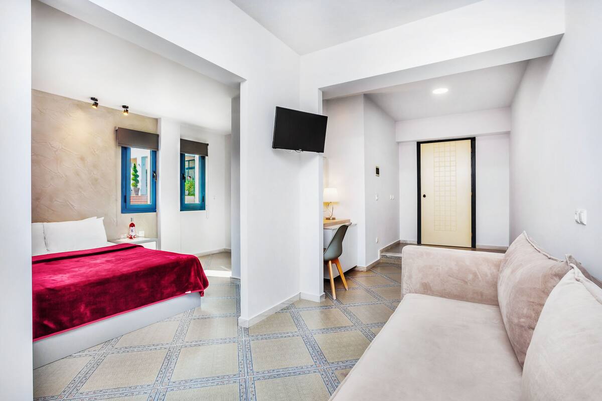 Una habitación de hotel moderna con cama, sofá, escritorio y televisor montado en la pared.