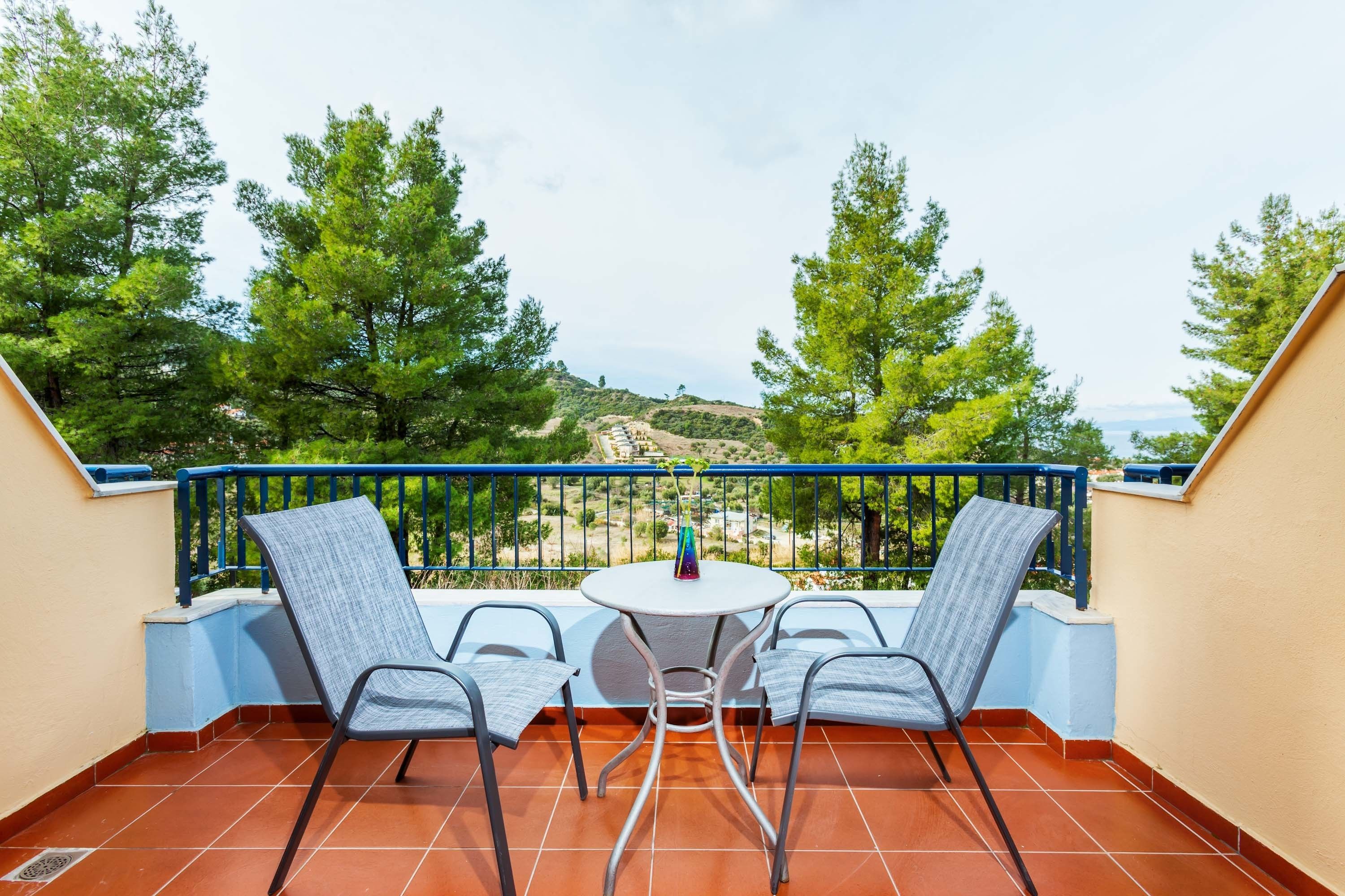A balcony with two chairs and a table, overlooking a scenic landscape with trees and hills.