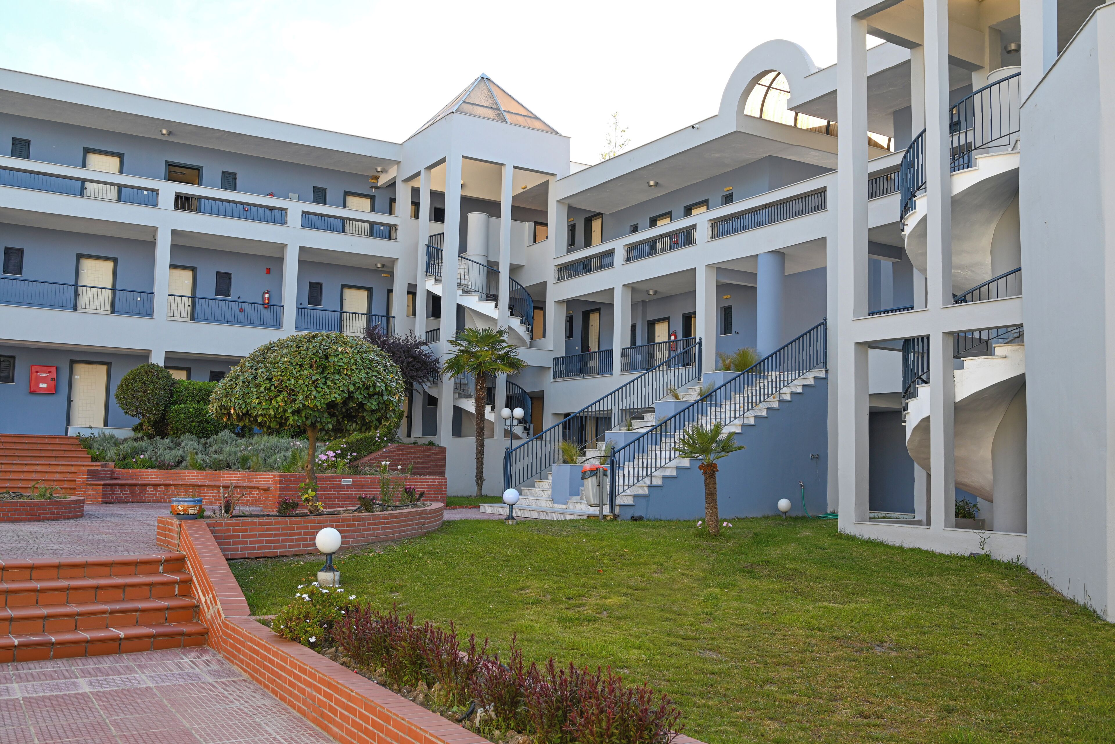 A multi-story hotel with a central courtyard, outdoor stairs, and a pool area.