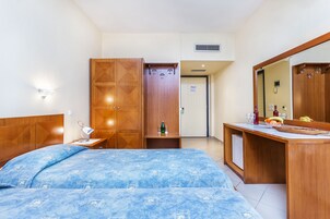 Habitación de hotel con cama, armario de madera, escritorio con espejo y una pequeña estantería con objetos personales.