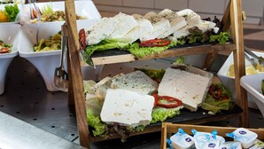 A buffet setup with multiple trays of food including cheese, vegetables, and possibly salads.