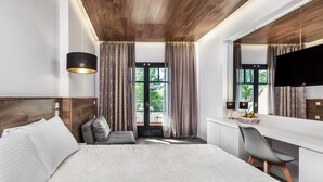 A modern hotel room with a large bed, a desk with a chair, a TV, and a balcony with curtains. - Atrium Hotel (Kassandra)