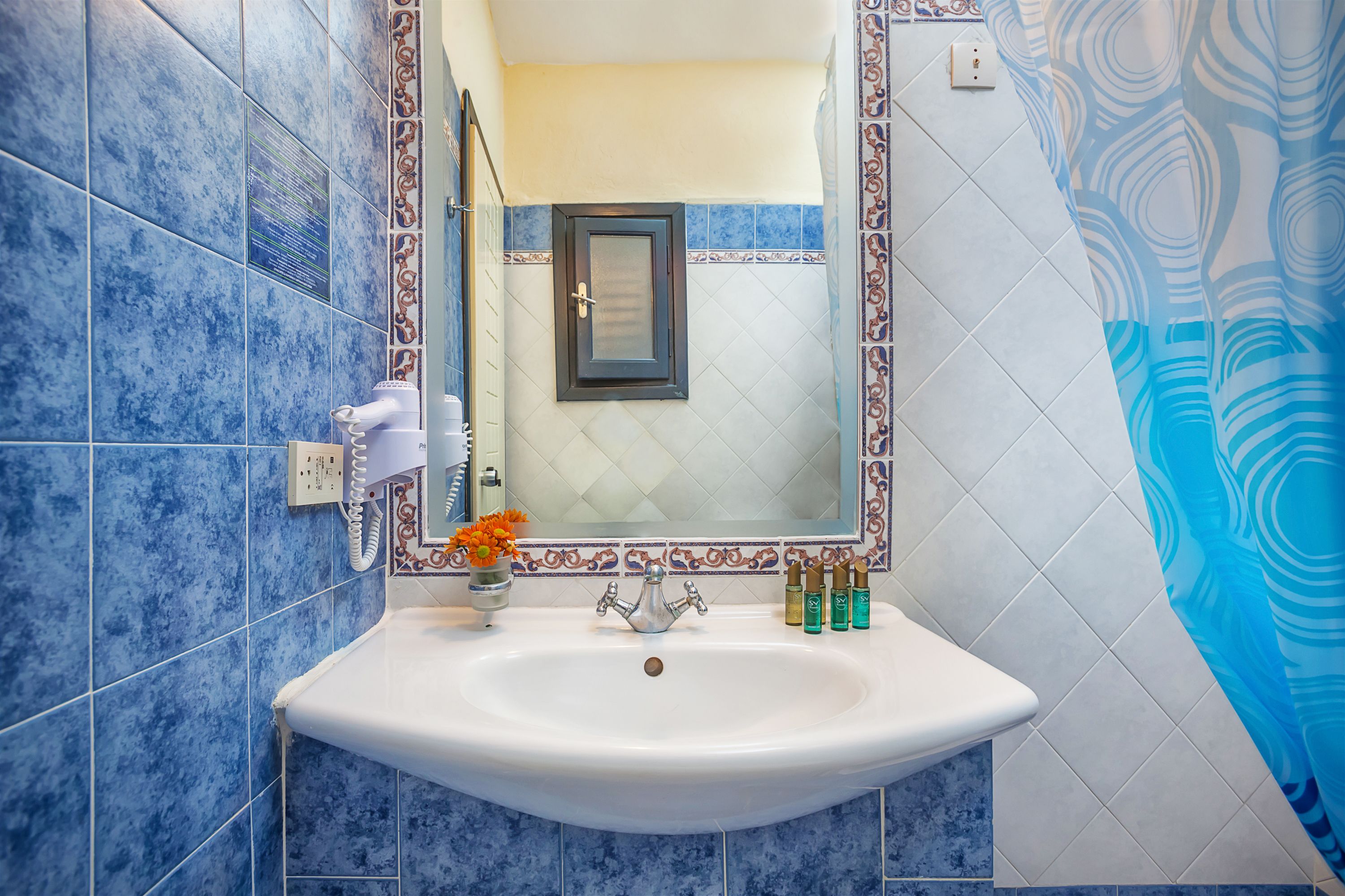 A bathroom with a white sink, blue patterned tiles, a mirror with a decorative frame, and a shower curtain with a blue abstract design.
