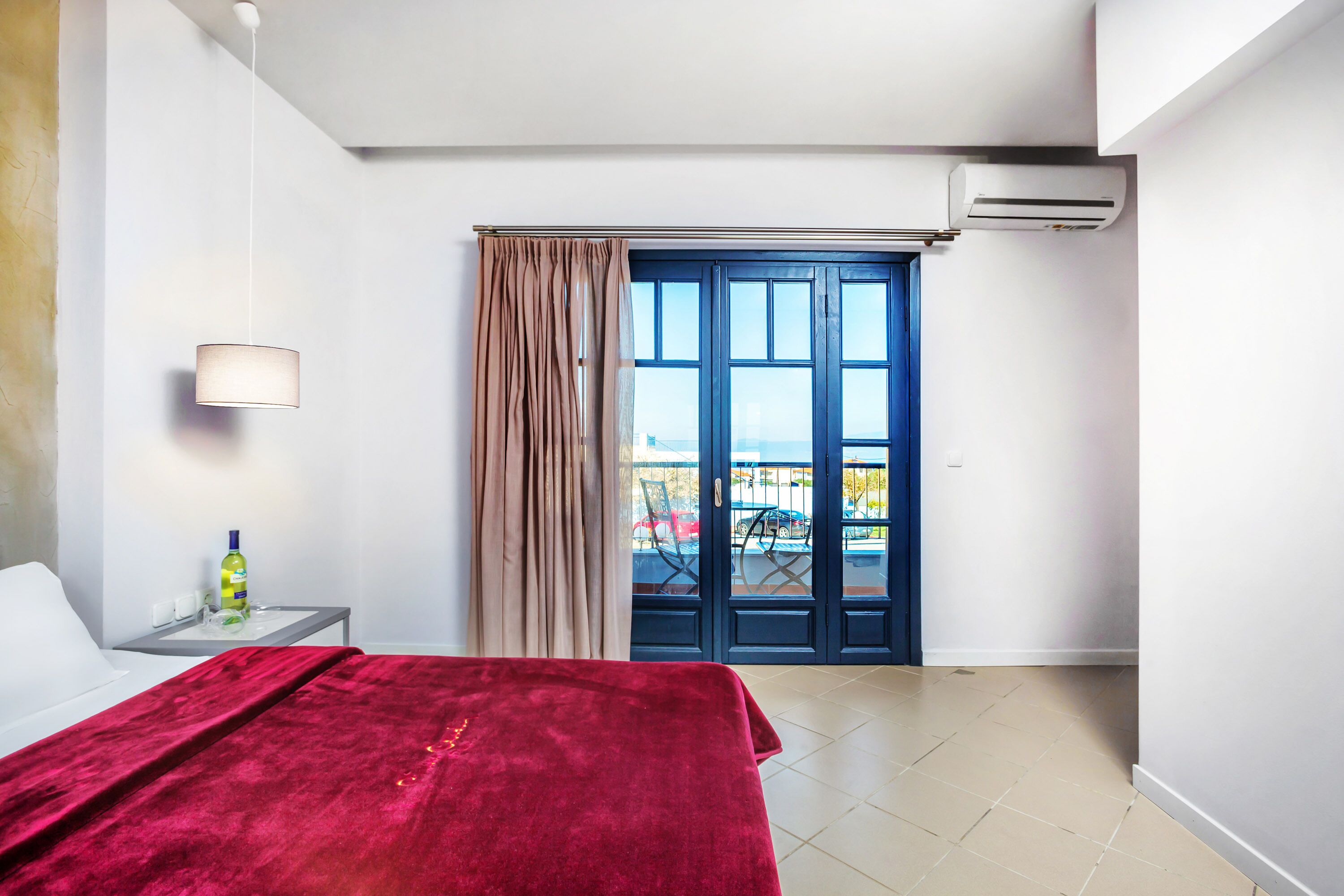 A hotel room with a bed, a nightstand, a lamp, a window with curtains, and an air conditioning unit.