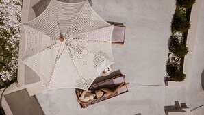 A top-down view of a room with a large woven umbrella, a wooden box, and a person lying on a mat. - Atrium Hotel (Kassandra)